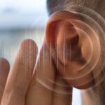 Imagem de um ouvido humano em close-up, com ondas sonoras digitais ilustradas ao redor, representando percepção auditiva ou captação de sons sutis